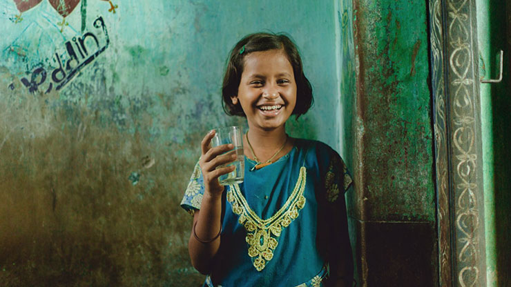 A smiling girl in a sari holding a glass of clean water