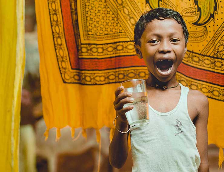 A boy laughing while holding a glass of clean water